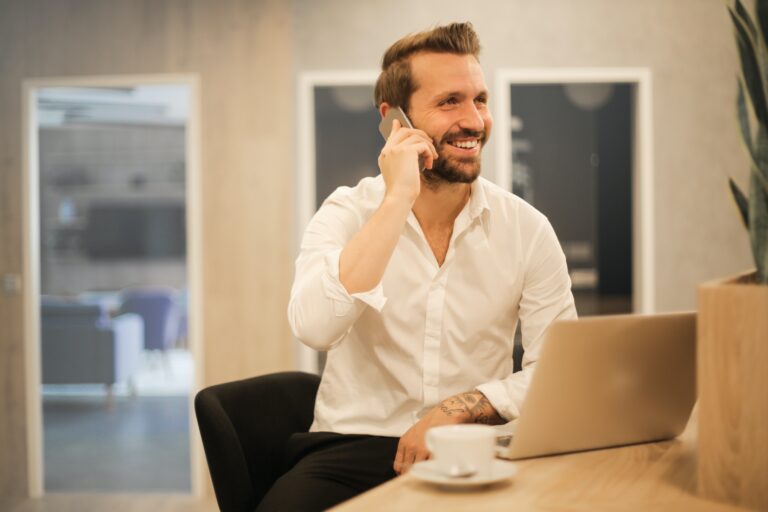 uomo in ufficio che sorride con laptop e cellulare, sta utilizzando jobby per ricerca di personale a chiamata